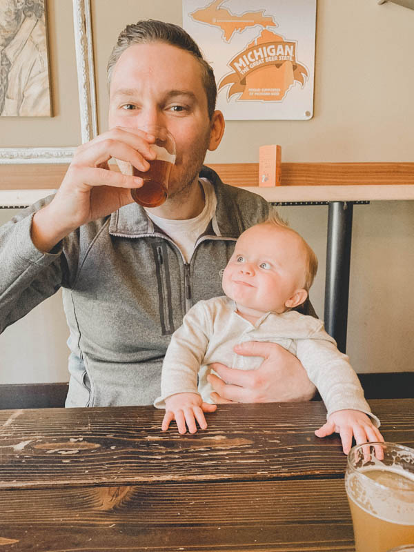 Guy drinking a beer with a baby at seven monks brewing co