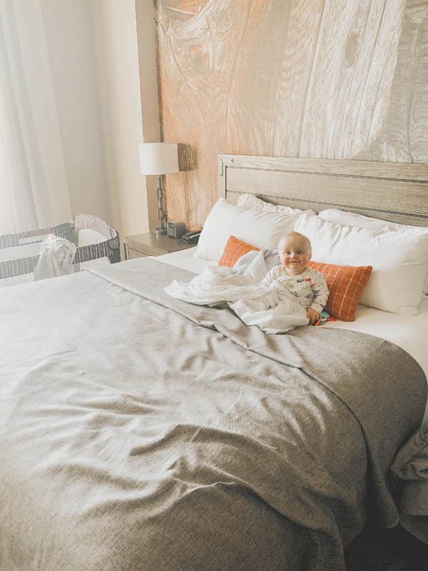 Baby sitting on a bed by themselves at a hotel.