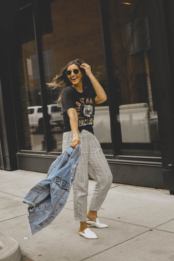 Girl standing on sidewalk wearing a graphic tee shirt, pants and a jean jacket