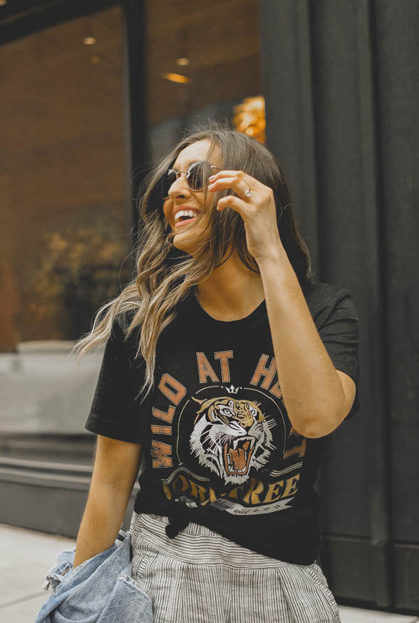 Girl standing on sidewalk wearing a graphic tee shirt, pants and a jean jacket