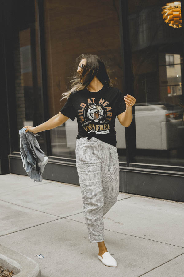 Girl standing on sidewalk wearing a graphic tee shirt, pants and a jean jacket