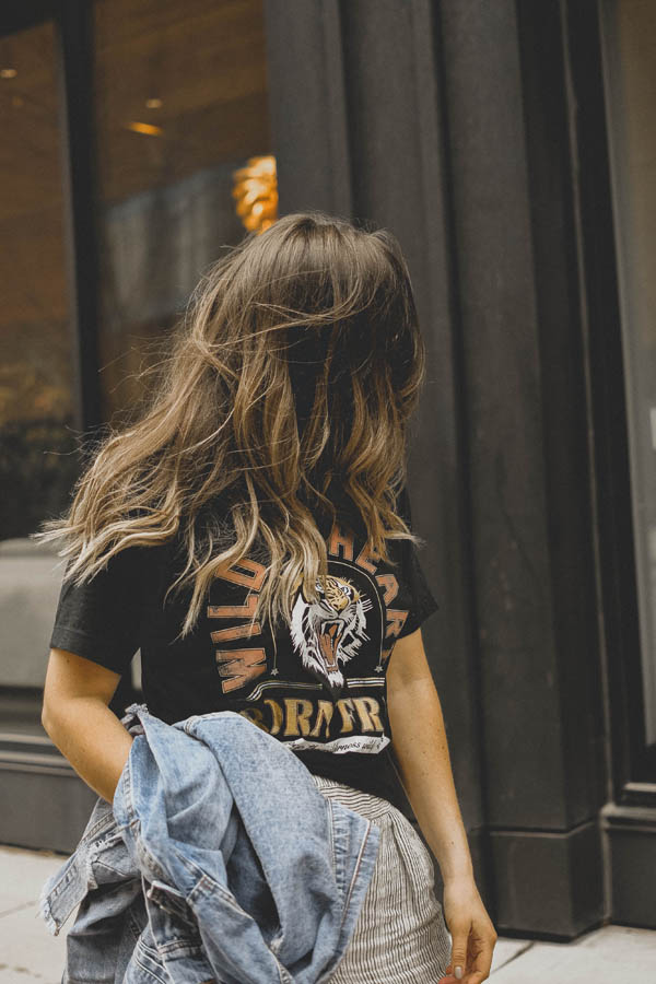 Girl standing on sidewalk wearing a graphic tee shirt, pants and a jean jacket