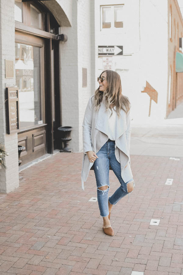 Girl Wearing A Spring Outfit a Light Colored Coat with Distressed Denim and Slides