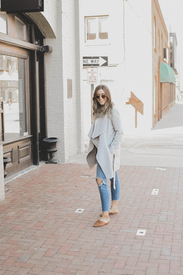Girl Wearing A Spring Outfit a Light Colored Coat with Distressed Denim and Slides