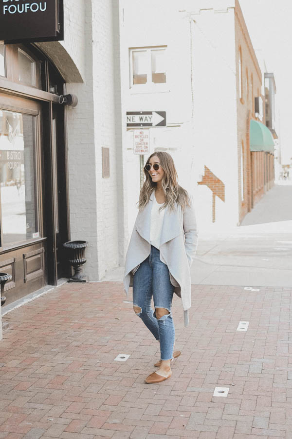 Girl Wearing A Spring Outfit a Light Colored Coat with Distressed Denim and Slides